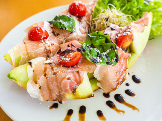 Fresh melon cantaloupe slices with prosciutto ham, balsamic vinegar sauce and basil in a plate on white background.