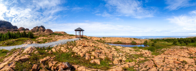 A giant panorama of the orange cliffs of the island of Leka on the shore of the blue sea under the blue sky. Footpath to the observation gazebo. Norway.