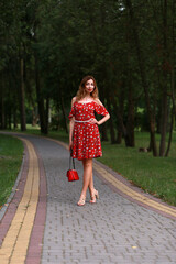 Slender woman in red dress standing  in the park