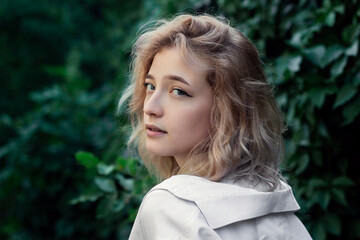 Portrait of a beautiful woman in white clothes on a background of green leaves