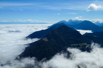 A panoramic view from the top of Alpine peak in Austria. The whole area is shrouded in thick clouds. A few peaks popping out from the clouds. High mountain chains in the back. Carpet from the clouds