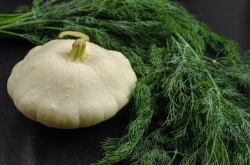 Minimalist composition with one Pattypan squash and a bunch of green dill on the black background....