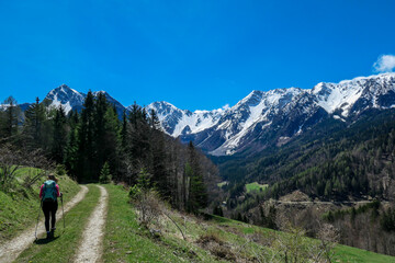 Fototapeta na wymiar A woman trekking with a backpack on a hiking trail with the view on Baeren Valley in Austrian Alps. The highest peaks in the chain are snow-capped. A few trees on the slopes. Sunny day. Wanderlust