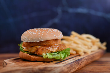 Home made hamburger with lettuce and cheese and fried potatoes on a wooden table.