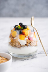 Greek yogurt with granola and fruits in jar on white marble background, copy space. Healthy food
