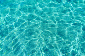 Turquoise Pure clear water in the sea, sun glare, waves and sea sand. Calm sea water background