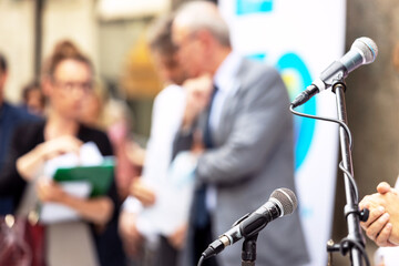 Microphone in focus at news conference or business presentation, blurred people in the background