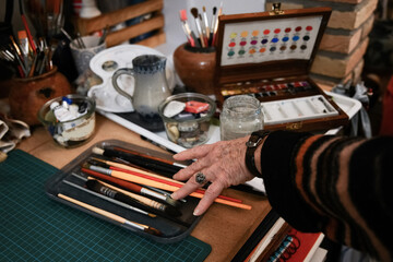 Old woman's hand takes paintbrushes for watercolor painting