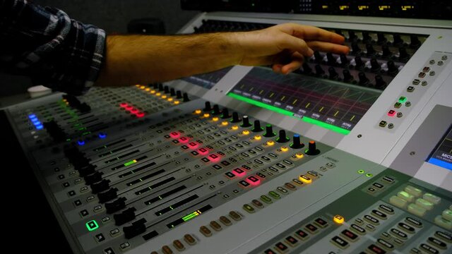Sound engineer is moving levers of a multitrack mixing console in the control room during a recording session