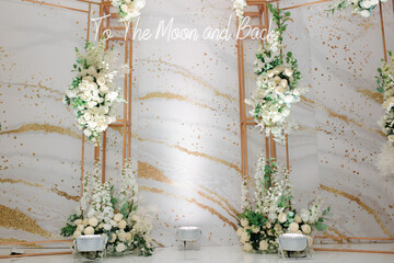 Wedding photo zone decorated by white flowers and green leafs with an inscription, To The Moon and Back