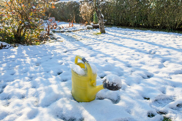 A yellow watering can stands in the snow-covered garden