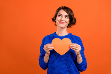 Photo of flirty brunette millennial lady hold heart look empty space wear blue pullover isolated on orange color background
