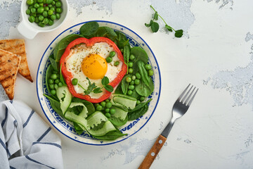 Red bell peppers stuffed with eggs, spinach leaves, green peas and microgreens on a breakfast plate on light grey table background. Top view.