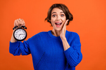 Photo of impressed brunette hair young lady hold clock wear blue sweater isolated on orange color background