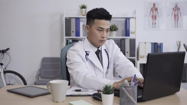 fast forward asian professional medical worker is using a touchpad while busy working writing report with laptop and receiving phone calls in a hospital office.