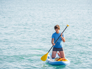 Handsome paddle boarder. Sportsman on knees paddling on stand up paddleboard. SUP surfing. Active...