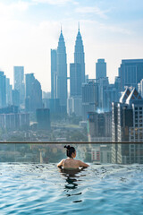 Naklejka premium young Asian woman enjoying in hotel roof top swimming pool, city view with blue sky for vacation travel, lifestyle of beautiful tourist girl with luxury outdoor skyscraper, Kuala Lumpur, Malaysia