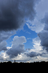 Gap in white and grey cumulus clouds showing patch of blue sky on a rainy day in summer
