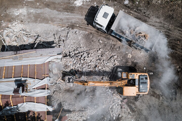Demolition of building by industrial excavator. Bucket breaks walls and roof of old house full of dust, aerial view.