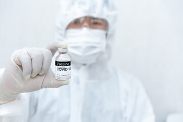 Medical laboratory technician wearing chemical protective Clothing holding syringe and COVID-19 vaccine in the laboratory