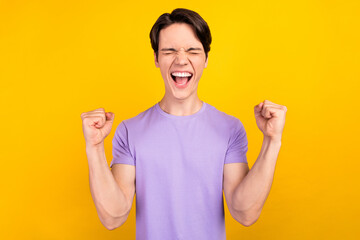 Photo of astonished champion guy raise fists close eyes scream wear purple t-shirt isolated yellow...