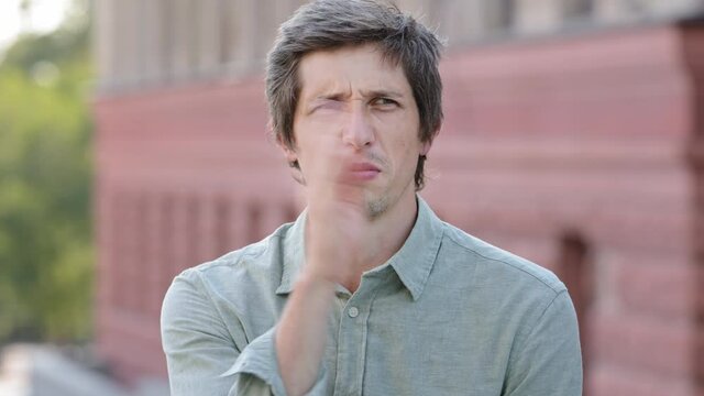 Headshot closeup portrait unhappy young Caucasian guy sniffing air closing nose holding breath. Millennial man suffering from unpleasant stinky intolerable disgusting smell avoiding nasty strong odor