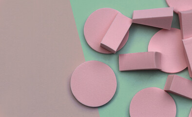 Pink make up application sponges in various sizes and shapes. Green and beige background with copy space