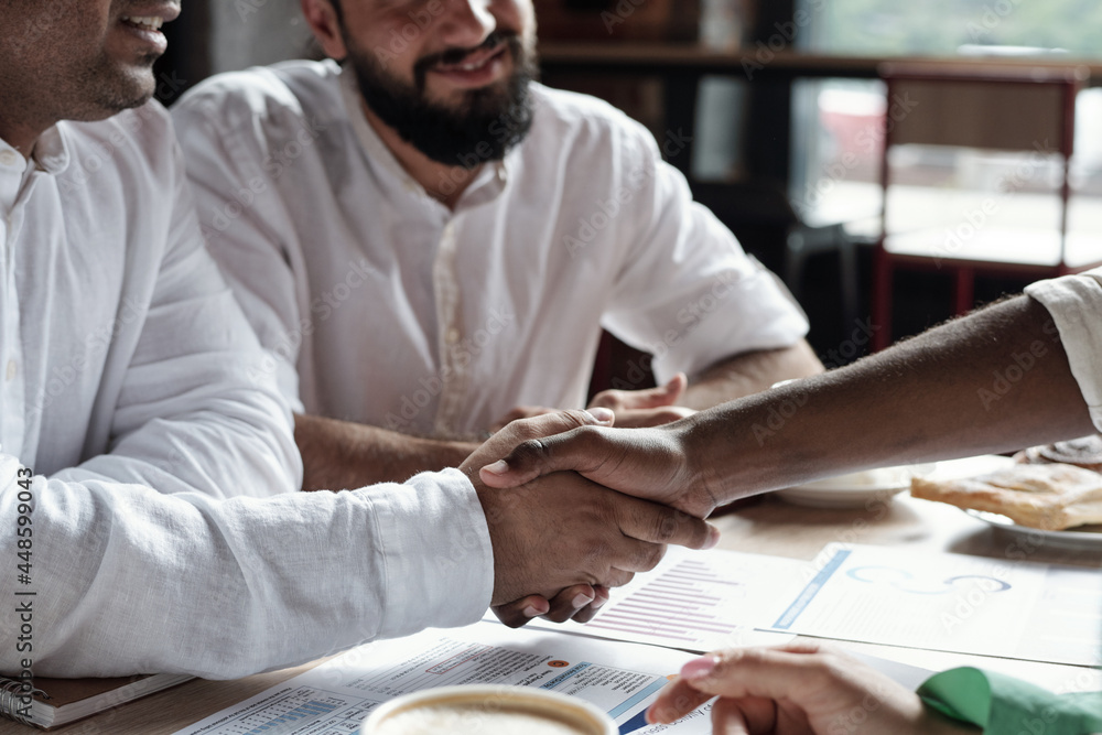 Wall mural Two Muslim businessmen shaking hands over financial papers on workplace