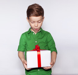 Surprised cute boy in a green shirt is happy with a gift in his hands with a red ribbon. Christmas gift box