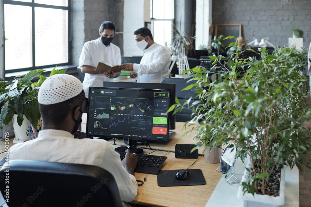 Poster rear view of young muslim businessman sitting in front of computer monitor and his two colleagues in