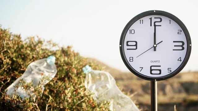 Time is running out. Clock ticking showing twelve o' clock. Plastic water bottle abandoned on nature. Environmental pollution global ecological problem.