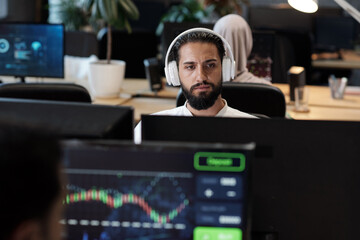Bearded Arabic businessman in headphones looking at computer screen in office environment