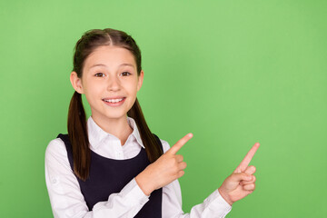 Photo of young school girl happy positive smile indicate fingers empty space ad advise promo isolated over green color background