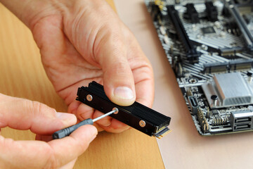 Fototapeta premium Hands with screwdriver hold and fix cooling radiator on memory device M2 NVMe to install in motherboard to computer