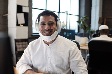 Fototapeta na wymiar Young successful mixed-race businessman in headphones looking at you with toothy smile