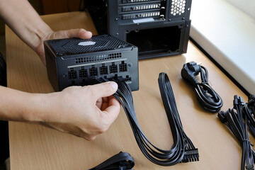Hands connect wires to power supply unit while assembling computer system - obrazy, fototapety, plakaty