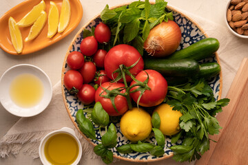 Salad ingredients (tomatoes, cucumbers, fresh basil, cherry tomatoes, onions, mint, parsley) in a large bowl. With olive oil, lemon, lemon juice and almonds. Persian salad. Preparation for meal. 