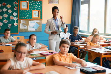 African American teacher with touchpad giving lecture to her students at elementary school.