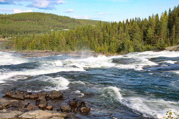 Storforsen is a waterfall on the Pite River in Swedish Norrbottens län. Beautiful view of the water flowing, and trees in the background on a summer day with blue sky. Near Lulea, Sweden.