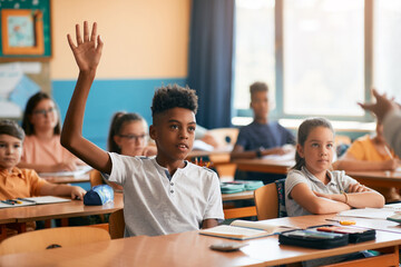 African American schoolboy raising his arm to answer teacher's question during class at school.