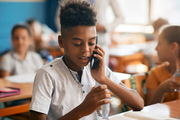 Black schoolboy talking on mobile phone during class in the classroom.