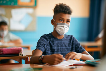 African American elementary student wearing protective face mask while learning in classroom at school.