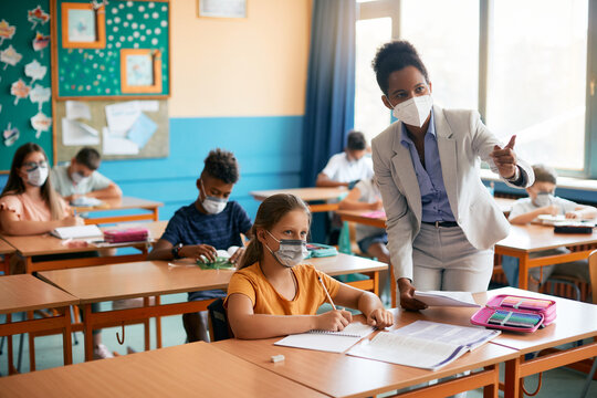 Black teacher and elementary students wearing protective face masks during class at school.