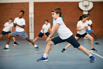 Elementary student and his friends warming up during PE class at school gym.