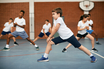 Fototapeta premium Elementary student and his friends warming up during PE class at school gym.
