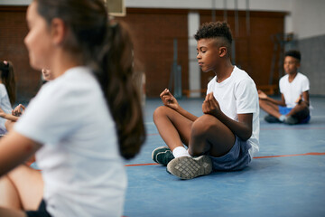 African American student meditating with eyes closed during PE class at school gym.