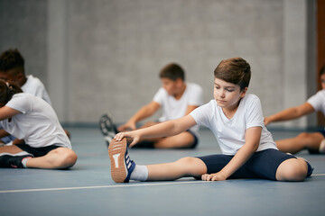 Elementary student stretching on floor during PE class at school gym.