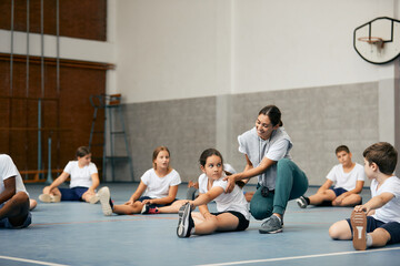 Happy female PE teacher having class with group of elementary students at school gym.
