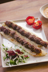grilled meat lamb shish kebab with vegetables, mezzes and salads on wooden table. adana, urfa kebap. turkish barbecue.