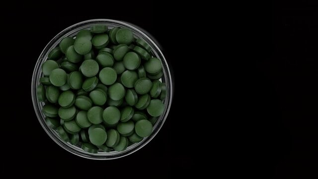Green pills on black background. superfoods Spirulina, chlorella supplement green pills top view rotation. 4K UHD video
